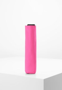 Parapluie rose au design élégant et allongé, fabriqué en tissu lisse ; présente une poignée noire en haut et une forme compacte pour la portabilité.