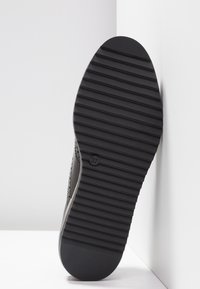 Semelle en caoutchouc noir avec des rainures horizontales et un marquage circulaire de taille. La tige de la chaussure est en matériau gris avec de petites perforations.