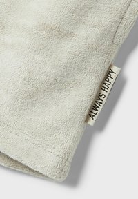 Lys beige håndklæde med en struktureret, blød overflade. Har et mærke, der står "ALWAYS HAPPY" i sort, sydd ind i hjørnet.