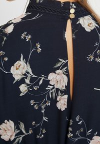 Närbild av en mörk blommig klänning med en nyckelhålsöppning i ryggen, prydd med rosa rosor och fina vita blommor.