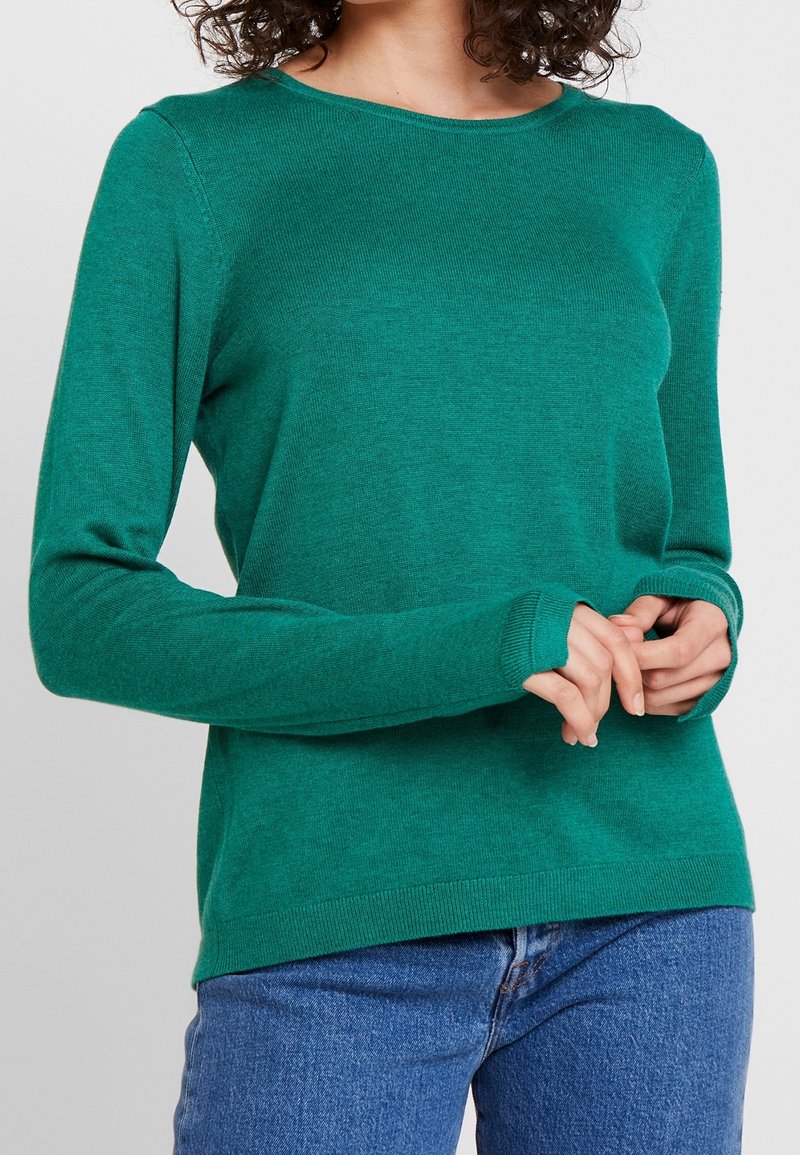 Pull vert à manches longues avec un col rond, en tissu doux. Doté de poignets et d'un ourlet côtelés, associé à un jean bleu clair.