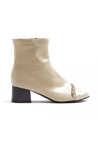 Beige lakované kotníkové boty se čtveratou špičkou, nízkým blokovým podpatkem a dekorativním řetízkem přes přední část. Hladký povrch a elegantní design.