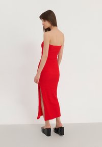 Röd, axelbandslös midi-klänning med texturerad tyg, slim fit, sidsprund och en figurnära livstycke, bärs med svarta platåsandaler.