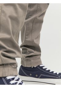 Beige pants with elastic cuffs worn over navy blue canvas sneakers with white laces and rubber soles on a light background.