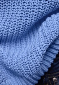 Gros plan sur un tissu tricoté bleu clair avec des motifs côtelés et texturés, montrant des boucles de fil et des plis détaillés.