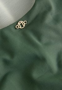 Maslinasto zeleni materijal s glatkom teksturom, s mrežastim dijelom i malim zlatnim okruglim kopčanjem na donjoj strani.