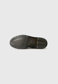 Black shoe sole with textured grip pattern and transparent midsection showing crisscross design on a white background