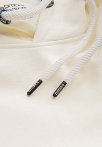 Gros plan sur le tissu d'un sweat à capuche blanc avec des cordons blancs ornés d'embouts en plastique noirs imprimés "OMBRE."