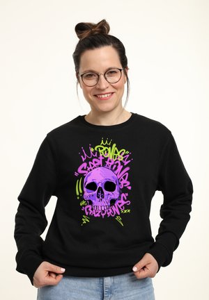 Černá mikina s grafickým designem, který zobrazuje purpurovou lebku a živé zelené a růžové graffiti písmo. Měkká textura, uvolněný střih.