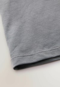 Grå bomulds T-shirt med en glat tekstur, der har en foldet ærme og en syet kant. Simpelt design, uden mønstre eller accenter synlige.