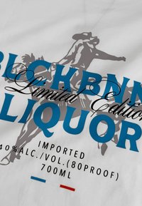 Het flesontwerp heeft een wit etiket met blauwe en zwarte tekst, een grijze silhouet van een ruiter, en rode en blauwe accenten aan de onderkant.