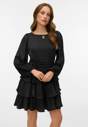 Melnas kleitas ar garām pūkainām piedurknēm, pieguļošu vidukli un daudzslāņu volānu svārku. Izgatavota no gludas auduma ar vienkāršu apaļu izgriezumu.