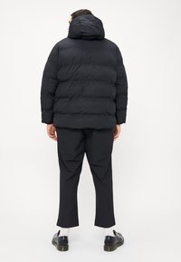 Crna puf jakna s kapuljačom, s kviltanim dizajnom i elastičnim manžetama. Nosi se uz tailored crne hlače i crne cipele.