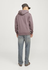Purple hooded sweatshirt with a relaxed fit, featuring a kangaroo pocket and ribbed cuffs, paired with light blue jeans and brown sandals.