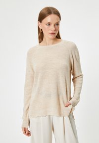 Beige stickad tröja med rund hals, lång ärm och ett strukturerat mönster. Har sidslitsar och detaljer på framfickorna.