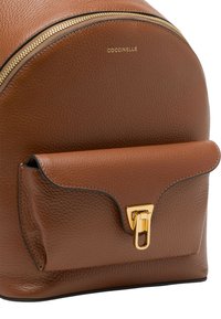 Zaino in pelle marrone con cima arrotondata, dotato di una tasca anteriore e accessori in tonalità oro. Superficie testurizzata con cuciture a contrasto.