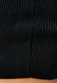 Svart ribbat tyg med vertikala ränder, med en strukturerad yta och en sömdetalj i mitten. Elastisk och figurnära design.