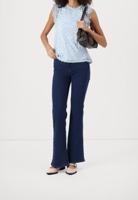 Ljusblå spetsblus med scallopärmar, mörkblå utsvängda jeans och beige ballerinas. Outfiten kompletteras av en liten brun axelväska.