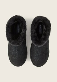 Schwarze Hausschuhe mit einem plüschigen, fellartigen Kragen und einem weichen Wildleder-Außenmaterial. Verfügt über ein glitzerndes Muster auf der oberen Fläche. Rund designte Zehenpartie.