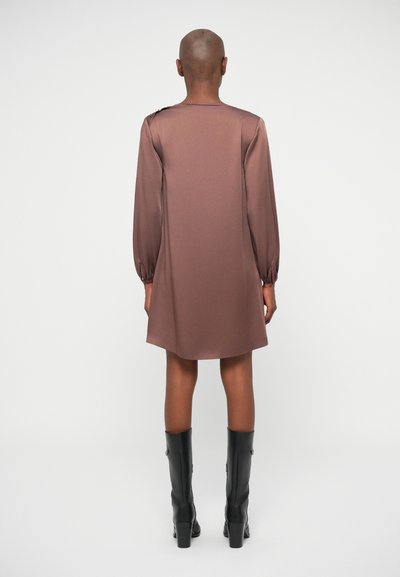 Robe marron à manches longues en matière lisse, avec des poignets élastiques et une coupe décontractée, associée à des bottes noires montant jusqu'aux genoux.