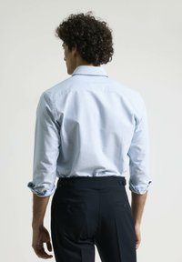 Camisa a rayas azul claro con cuello regular, mangas enrolladas y textura suave, combinada con pantalones oscuros ajustados con presillas para cinturón.