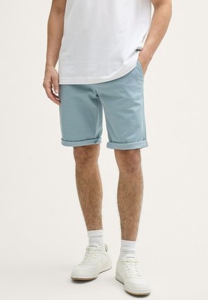 Shorts roulés bleu clair en tissu mélange coton, dotés de poches latérales, associés à un t-shirt blanc et des baskets blanches.
