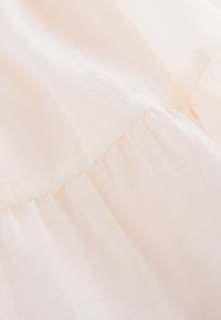 Šviesiai rožinė medžiaga su minkštu, tekstūruotu paviršiumi, išryškinanti surinktą siūlės detalę. Medžiaga atrodo lengva ir permatoma.