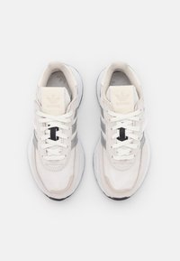 Vita canvasträningsskor med grå ränder, rund tå, vita snören och strukturerad gummisula. Har diskret varumärkning på tungan.