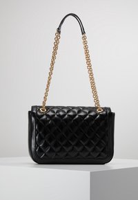 Svart kviltad läderhandväska med rektangulär form, gyllene kedjesnor och cirkulära metalldetaljer. Slät textur, minimalistisk design.