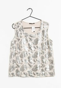 Top beige sans manches avec motifs de feuilles en sequins argentés, suspendu à un cintre noir sur un fond blanc.