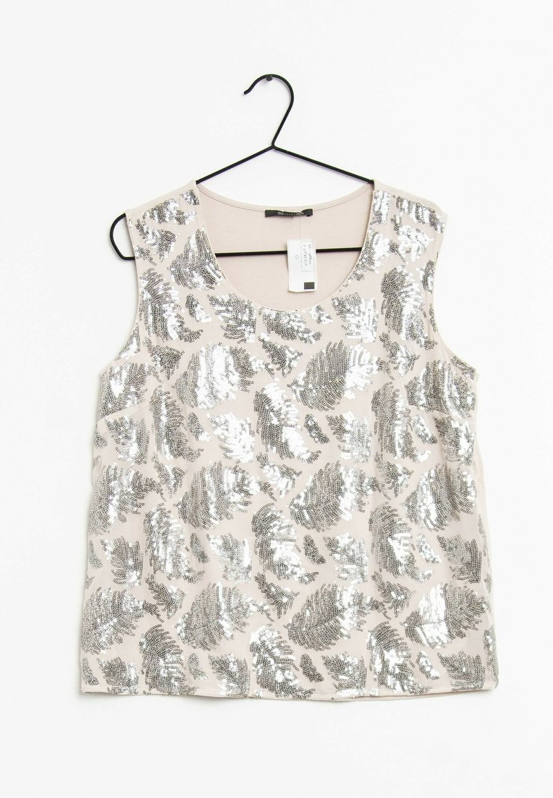 Top beige sans manches avec motifs de feuilles en sequins argentés, suspendu à un cintre noir sur un fond blanc.