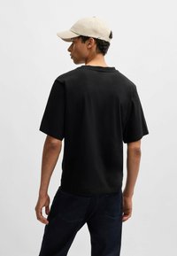 Czarna koszulka z krótkim rękawem o okrągłym dekolcie, płaskim wykończeniu i luźnym kroju, w połączeniu z ciemnymi dżinsami. Wygląd dopełnia jasnobeżowa czapka.