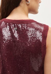 Bordový tielkový top s pletenou textúrou a flitrami na chrbte, doplnený malou značkovou štítkou pri výstrihu.