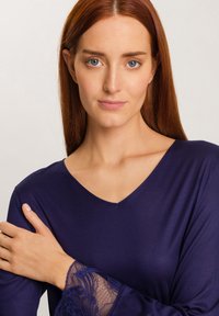 Top blu navy con scollatura a V e maniche lunghe, caratterizzato da dettagli in pizzo trasparente ai polsini. Texture liscia con design aderente.