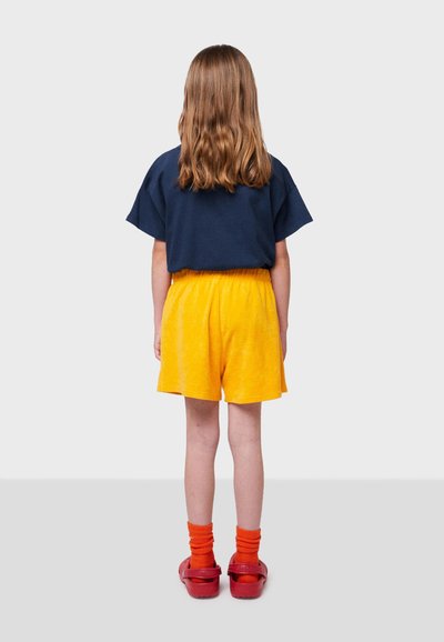 Marinblå t-shirt med kort ärm, gula shorts och röda träskor med orangea strumpor. Utsikt bakifrån, med en avslappnad passform och mjuk textur.