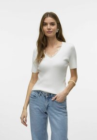 Witte geribbelde top met korte mouwen en een gegolfde kanten halslijn. Gecombineerd met lichtblauwe high-waisted jeans. Eenvoudig, aansluitend ontwerp.