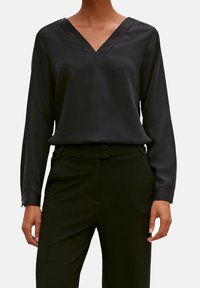 Blusa nera a V con maniche lunghe, texture liscia e dettagli di cucitura sottili. Abbinate a pantaloni neri slim.