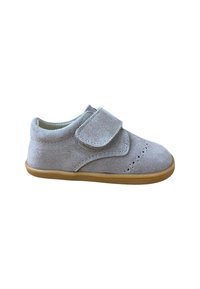 Zapato de bebé de ante gris claro con cinta de Velcro, detalles perforados en la punta y suela de goma marrón clara, aislado sobre fondo blanco.