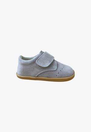Zapato de bebé de ante gris claro con cinta de Velcro, detalles perforados en la punta y suela de goma marrón clara, aislado sobre fondo blanco.