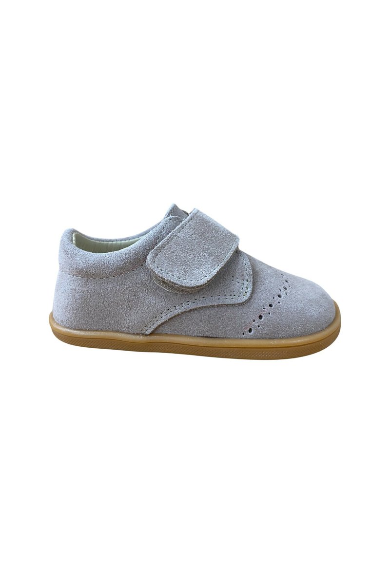 Zapato de bebé de ante gris claro con cinta de Velcro, detalles perforados en la punta y suela de goma marrón clara, aislado sobre fondo blanco.