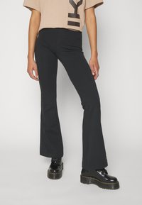 Fekete harangnadrág rugalmas anyagból, közepes magas derékkal. Fekete platform csizmával és bézs grafikus pólóval párosítva.