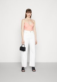 Top curto rosa com detalhe de anel central, combinado com calças brancas de perna larga de cintura alta. Mala de mão mini preta e sandálias de salto pretas.