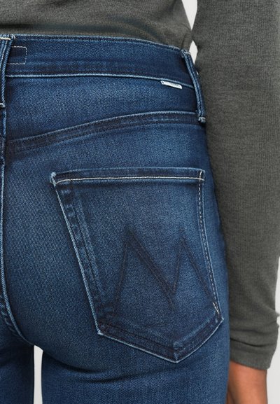 Jeanși din denim de culoare albastru închis cu talie înaltă, textură ușor decolorată și un model distinctiv cu literă "M" cusut pe buzunarul din spate.