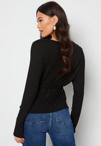 Top nero a coste con maniche lunghe, vita aderente con cinturino, e scollatura rotonda, abbinato a jeans blu a vita alta con un design testurizzato.