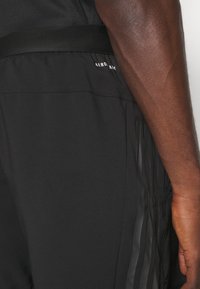 Svarta sportshorts i lätt material, med en slät yta, ett tonalt randmönster och ett elastiskt midjeband med en logotyp.