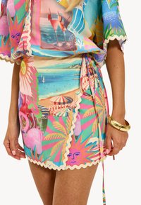 Robe colorée et à motifs tropicaux, avec des bords en forme de coquille et un lien sur le côté. Fabriquée en tissu léger, de longueur courte.