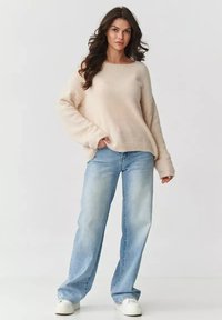 Jasno-beżowy, puszysty sweter z długimi rękawami, w połączeniu z luźnymi, jasnoniebieskimi dżinsami i białymi sneakerami. Prosty design i luźny krój.