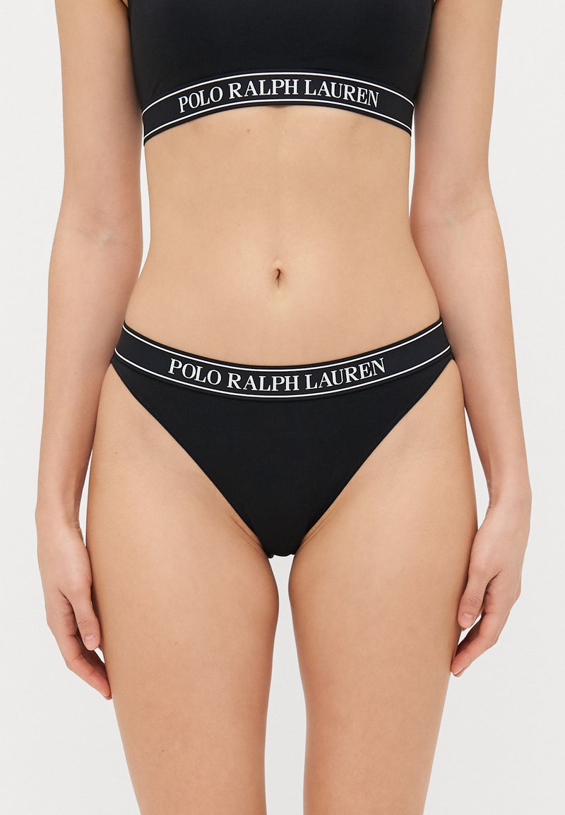 Melna bikinija komplekts ar ribotu tekstūru. Augšdaļai ir bieza josta ar "POLO RALPH LAUREN" baltā krāsā, kas atbilst bikini apakšdaļas jostai.