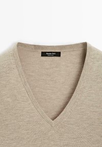 Hellbeige V-Ausschnitt Pullover mit glatter Textur und einem Etikett mit der Aufschrift "Massimo Dutti", vor einem weißen Hintergrund platziert.