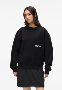 Felpa nera oversize in tessuto di cotone, con scollatura a girocollo e polsini a coste. Testo del logo bianco sulla parte frontale.